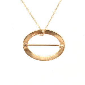 May include: A gold circle pendant necklace with a clasp on the back. The pendant is a circle with a bar across the center.