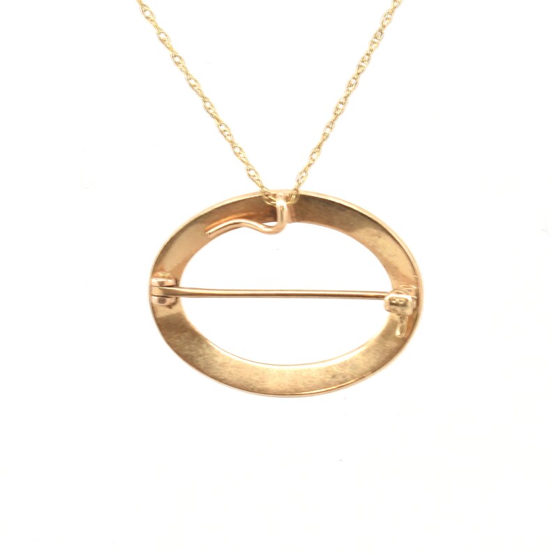 May include: A gold circle pendant necklace with a clasp on the back. The pendant is a circle with a bar across the center.