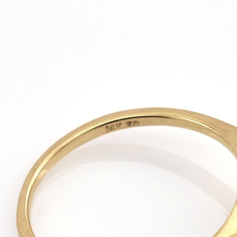 May include: A polished yellow gold ring band featuring a smooth, curved surface. The interior of the band is clearly stamped with the text 14K 50, indicating the metal purity and specific hallmark of the jewelry piece in a clear, legible font.