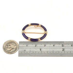 May include: An oval-shaped brooch with a blue enamel design and a row of pearls around the edge. The brooch is 1 1/2 inches long and is made of gold.