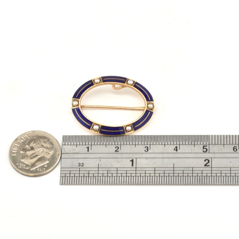 May include: An oval-shaped brooch with a blue enamel design and a row of pearls around the edge. The brooch is 1 1/2 inches long and is made of gold.