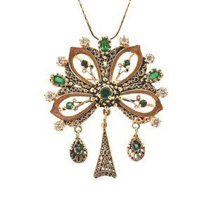 May include: A gold pendant necklace with a filigree design featuring green and white gemstones. The pendant is shaped like a stylized tree with three dangling drops.