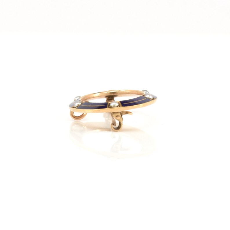 May include: A gold ring with a blue enamel design and pearl accents. The ring is on a white background.