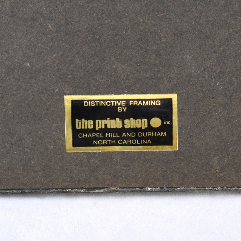 May include: A gold label with the text "DISTINCTIVE FRAMING BY the print shop inc. CHAPEL HILL AND DURHAM NORTH CAROLINA" on a black background.
