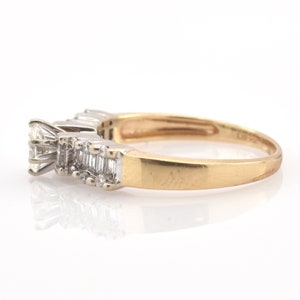 May include: A gold ring with a series of diamonds. The ring features a large, square-cut diamond at the front, followed by a row of smaller, rectangular-cut diamonds. The band is gold, and the diamonds are set in a white metal.