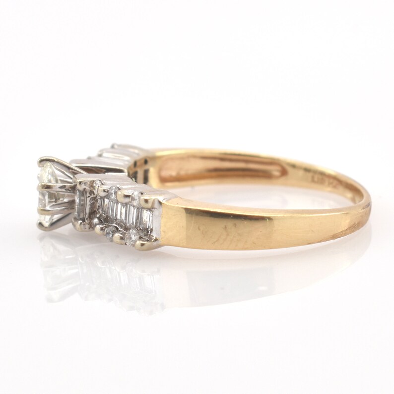 May include: A gold ring with a series of diamonds. The ring features a large, square-cut diamond at the front, followed by a row of smaller, rectangular-cut diamonds. The band is gold, and the diamonds are set in a white metal.
