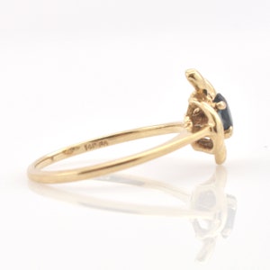 May include: A gold ring featuring a dark blue gemstone set in a prong setting. The band is thin and smooth, with the inscription 14K stamped clearly on the inner surface of the metal band. The design shows the side profile of the ring setting.