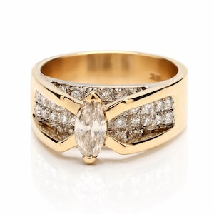 May include: A gold ring featuring a central marquise-cut diamond flanked by two rows of smaller round-cut diamonds set into the band. The polished gold band has a wide, tapered design that frames the center stone with smooth metal accents.
