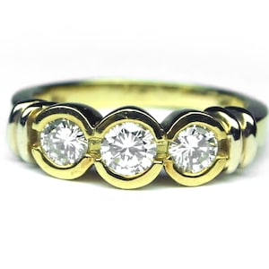 May include: A yellow gold ring featuring three round brilliant cut clear stones set in individual circular bezels. The band has a smooth, polished finish and a continuous design that highlights the three stones arranged horizontally across the top.