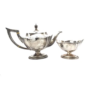 May include: A silver teapot and sugar bowl set with a fluted design. The teapot has a gold band around the handle and a monogram on the front. The sugar bowl has a matching monogram.
