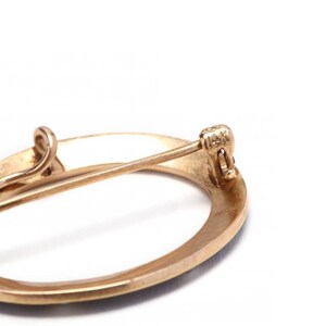 May include: A gold oval-shaped brooch with a pin closure. The back of the brooch is marked "14K".