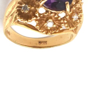 May include: A gold ring with a large, oval-cut purple gemstone and small diamond accents. The ring has an intricate, floral design around the main stone. The band is stamped with "14K".