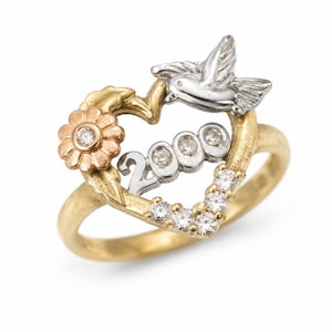 May include: A gold ring featuring a heart-shaped design with a dove, flower, and the number "2000". The ring has a gold band, a flower with a diamond center, and a dove with silver wings. The heart is adorned with diamonds.