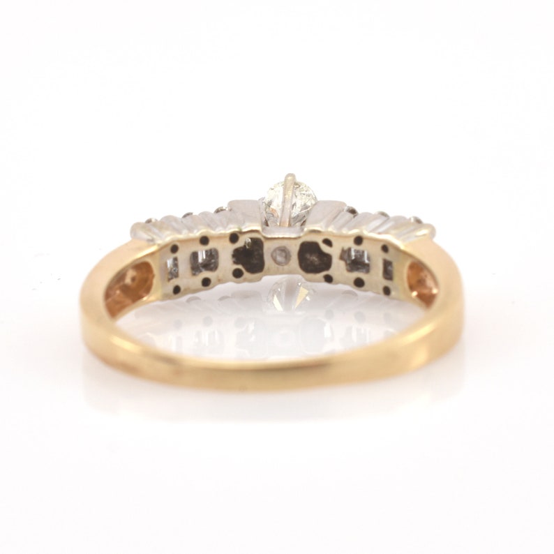 May include: A gold and silver ring with a central diamond and smaller accent stones. The ring has a classic design with a gold band and a silver setting for the diamonds. The ring is set against a white background.