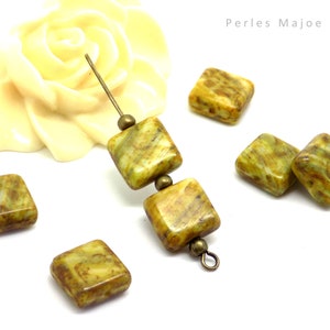 Puede incluir: Cuentas cuadradas en tonos verde oliva y marrón con efecto veteado, ensartadas con elementos metálicos. La imagen muestra cuentas sueltas y el texto "Perles Majoe". Ideales para bisutería.