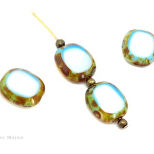 Può includere: Perline ovali con centro bianco, bordate di blu e marrone, infilate insieme. Le perline hanno un aspetto macchiettato e invecchiato. Una singola perlina è mostrata anche separatamente. Le perline sono su sfondo bianco.