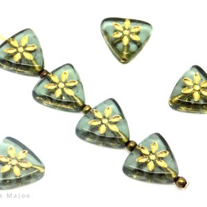 Op de afbeelding: Een streng driehoekige glazen kralen met gouden bloemaccenten. De kralen zijn geregen op een draad met bronzen afstandhouders.