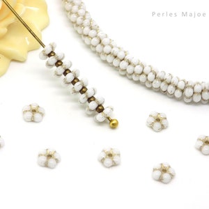 Peut inclure: Perles de fleurs en verre blanc avec des accents dorés. Les perles sont enfilées sur un fil et sont présentées sur une surface blanche. Les perles mesurent environ 6 mm de diamètre.
