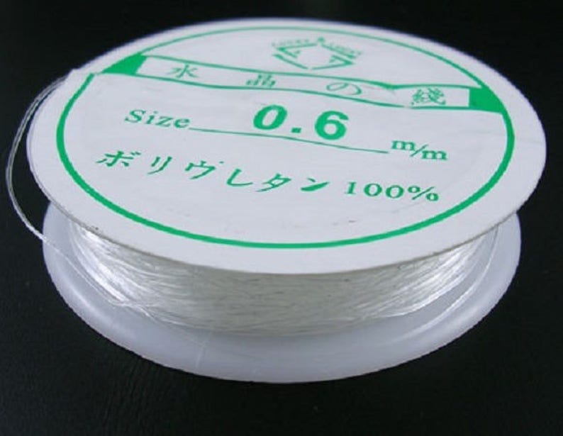 May include: A spool of white elastic cord with a green label that reads "Size 0.6 mm/m  Polyester 100%"