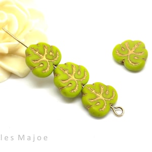 Könnte beinhalten: Vier grüne Glasperlen mit einem goldenen Blattdesign. Die Perlen sind auf einem Draht aufgefädelt und haben eine goldene Schlaufe am Ende.