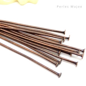 Peut inclure: Un lot d'épingles à tête plate en cuivre, posées sur une surface blanche.  Perles Majoe est imprimé dans le coin supérieur droit de l'image.