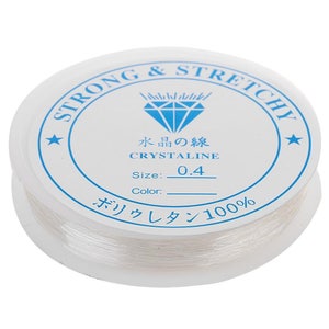 Peut inclure: Une bobine de fil élastique transparent étiquetée "STRONG & STRETCHY" avec un logo en forme de diamant et le texte "CRYSTALINE" en bleu. La taille est de 0,4 et le matériau est 100% polyuréthane.