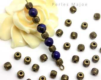 Pode incluir: Close-up de um fio de contas de lapis-lazúli azul com contas espaçadoras de ouro antigo. As contas espaçadoras são quadradas com um design floral em relevo. As contas estão espalhadas sobre uma superfície branca.