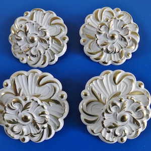 Peut inclure: Quatre rosettes décoratives en céramique blanche avec des accents dorés. Chaque rosette présente un motif floral avec un centre surélevé.
