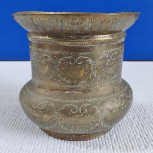 May include: A vintage brass vase with etched floral and bird patterns. The vase features a wide, flared rim and a rounded body, displaying detailed craftsmanship. The gold metallic colour enhances its antique aesthetic.