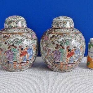 May include: Two antique Chinese porcelain ginger jars with intricate floral and figural designs in shades of pink, green, blue, and gold. The jars have a round shape and a lid.