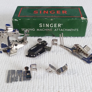 Może przedstawiać: Zestaw vintage akcesoriów do maszyny do szycia Singer w zielonym pudełku. Akcesoria są wykonane z metalu i mają srebrne wykończenie. Na pudełku widnieje napis "Singer Sewing Machine Attachments".