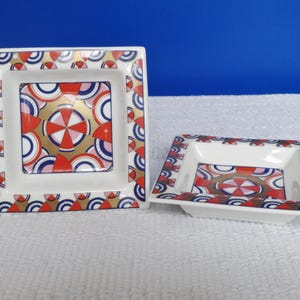 Peut inclure: Deux plats carrés en céramique avec un motif géométrique. Les plats sont blancs avec un motif rouge, bleu et or. Le plus grand plat mesure environ 13 cm de côté, et le plus petit mesure environ 8 cm de côté.