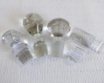 Peut inclure: Cinq bouchons de bouteille en verre transparent de formes et de tailles variées. Les bouchons sont en verre transparent et présentent une variété de textures.