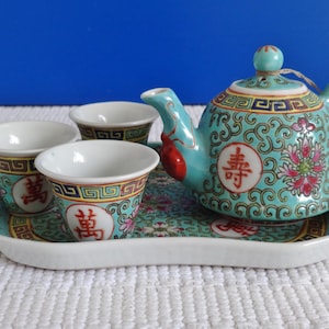 Puede incluir: Un juego de té de porcelana turquesa y blanco con una tetera, cuatro tazas y una bandeja. La tetera y las tazas tienen un diseño floral con caracteres chinos. La bandeja tiene un diseño floral con un borde dorado.