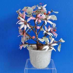 Op de afbeelding: Een delicate glazen bloemenarrangement in een groene keramische pot. De bloemen zijn gemaakt van roze, wit en groen glas en zijn in de vorm van een boom gerangschikt. De pot heeft een decoratief ontwerp.