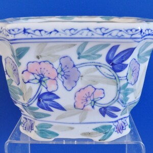 May include: A white ceramic planter with a blue and green floral design. The planter has a hexagonal shape and a scalloped rim.