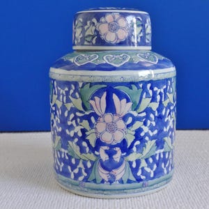 Könnte beinhalten: Eine blaue und weiße Porzellan-Dose mit Blumenmuster. Die Dose hat einen Deckel und ist mit rosa und grünen Blumen verziert.