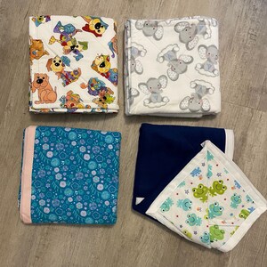 May include: Four different baby blankets. One is white with gray elephants, one is blue with white stars, one is teal with white flowers, and one is white with green frogs.
