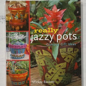 May include: A book titled "really jazzy pots: Glorious Gift Ideas" by Mickey Baskett. The cover features three decorated flower pots, one with a tropical leaf design, one with a birthday message, and one with a monogram.