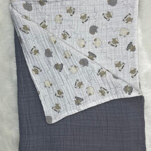 May include: A soft, gray and white baby blanket with a sheep pattern on one side. The blanket is made of a soft, breathable fabric and is perfect for cuddling.