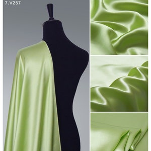 Könnte beinhalten: Ein hellgrüner Satin-Stoff, der über eine schwarze Schaufensterpuppe drapiert ist. Der Stoff ist glatt und seidig, mit einem dezenten Glanz. Der Stoff wird in drei verschiedenen Posen gezeigt, die seinen Fall und seine Textur hervorheben.