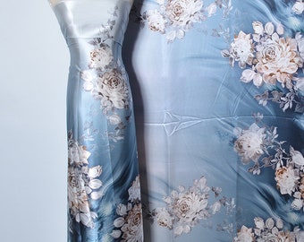 May include: A light blue satin fabric with a white floral print. The fabric is draped over a mannequin and a flat surface.