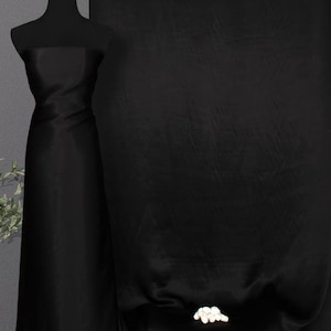 May include: Black fabric draped over a mannequin and a table. The fabric has a subtle sheen and a smooth texture.