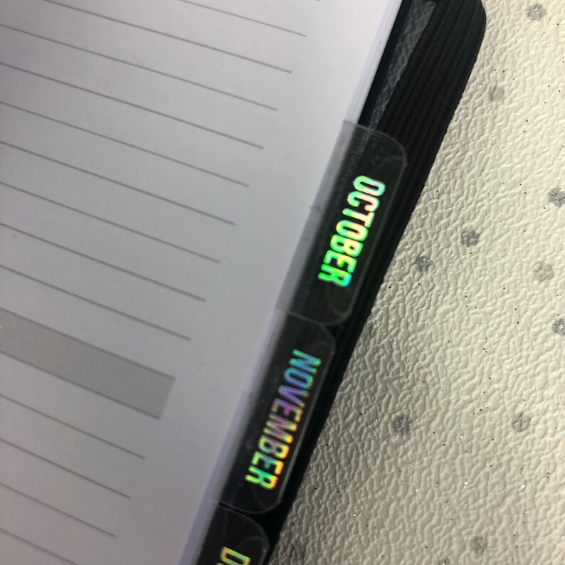 May include: Close-up of a black planner with iridescent tabs labeled "October" and "November".