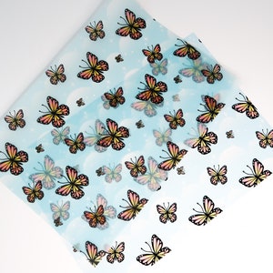May include: A sheet of translucent blue wrapping paper with a repeating pattern of orange and pink butterflies on a white background.