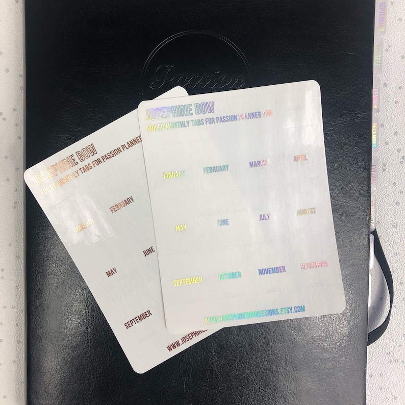 May include: Two sheets of clear, iridescent stickers with the text "Josephine Bow" and "Full Color Monthly Tabs for Passion Planner" printed on them. The stickers are labeled with the months of the year in rainbow colors.