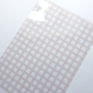 May include: A translucent sheet with a light pink and white gingham pattern. The grid design is composed of soft, brushstroke-style lines, creating a subtle, textured effect. The sheet is slightly angled, showcasing the pattern's repeating squares.