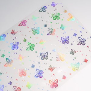 Può includere: Un foglio di vinile trasparente iridescente con un motivo ripetitivo di farfalle colorate. Le farfalle sono contornate d'argento e hanno una finitura olografica.