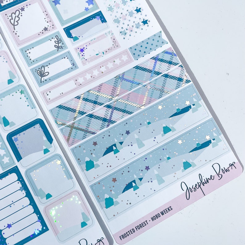 Puede incluir: Un conjunto de pegatinas para planificador con un tema de bosque de invierno en colores azul, blanco y rosa. Las pegatinas incluyen una variedad de formas, incluyendo estrellas, &aacute;rboles y patrones de cuadros. El texto "FROSTED FOREST - HOBO WEEKS" y "Josephine Bow" es visible en las pegatinas.