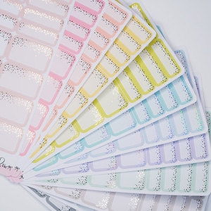 Puede incluir: Un conjunto de pegatinas rectangulares de colores con un borde brillante. Las pegatinas están dispuestas en forma de abanico y tienen un fondo blanco.